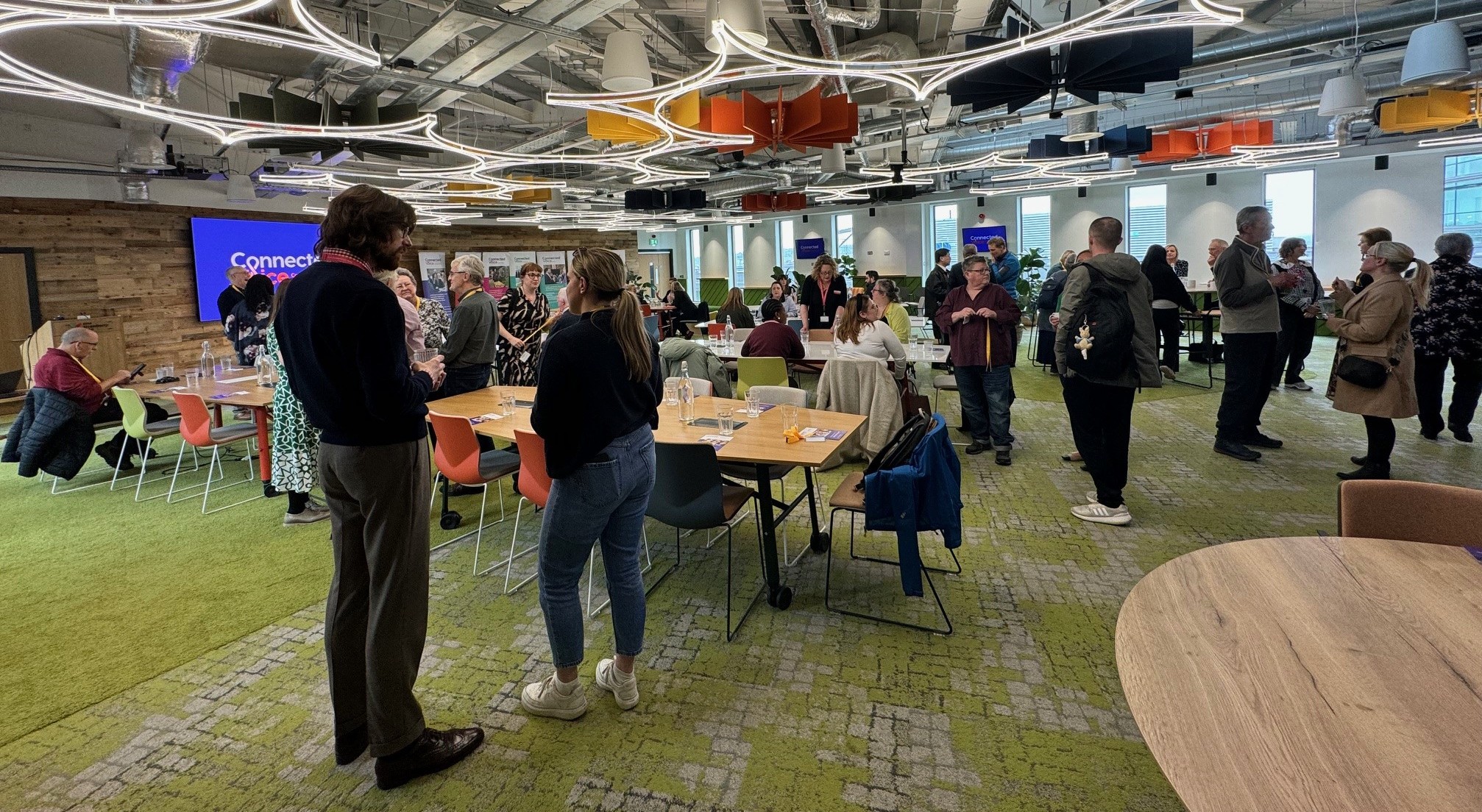 A large group of people in a meeting room chatting 