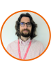 A head and shoulders shot of Giovanni, he has dark hair just above his shoulders, a beard, glasses, and is wearing a pink checked shirt